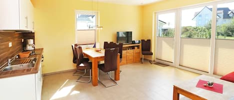 A compact living space with a dining area, kitchenette, and a sliding glass door leading to a balcony.