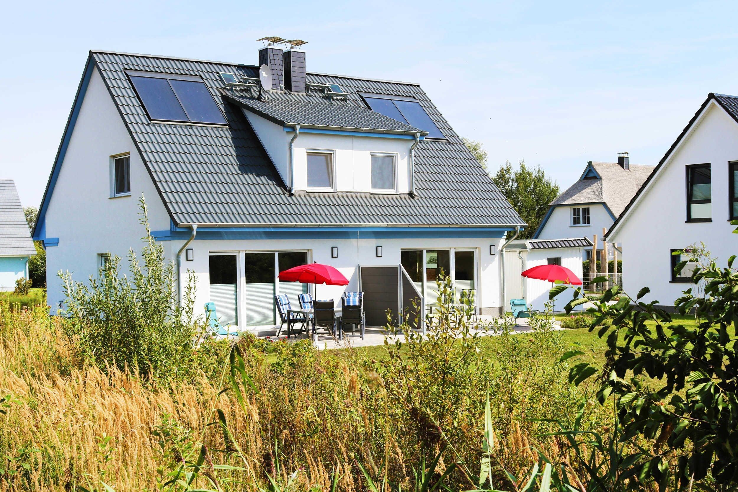 A two-story house with a sloped roof, solar panels, and a covered patio with outdoor furniture.