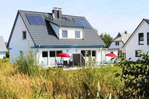 Et toetagers hus med skråtag, solpaneler og en overdækket terrasse med udendørs møbler.