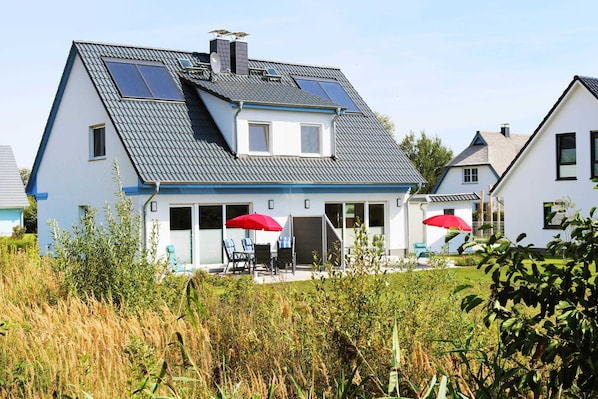 A two-story house with a sloped roof, solar panels, and a covered patio with outdoor furniture.