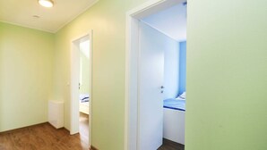 Ein Flur mit Holzboden, einem weißen Heizkörper und einer Tür zu einem Schlafzimmer mit Bett und blauer Wand.