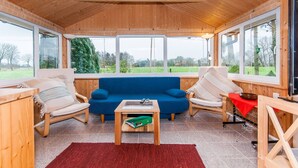 A cozy room with a blue sofa, two chairs, a small table, and large windows offering a view of the outdoors. - Ferienwohnung 'Hühnerstall' an der Nordsee (Stadland)