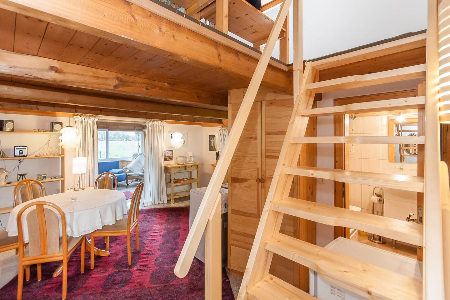 A wooden interior with a dining area, a staircase, and a view of the outdoors.