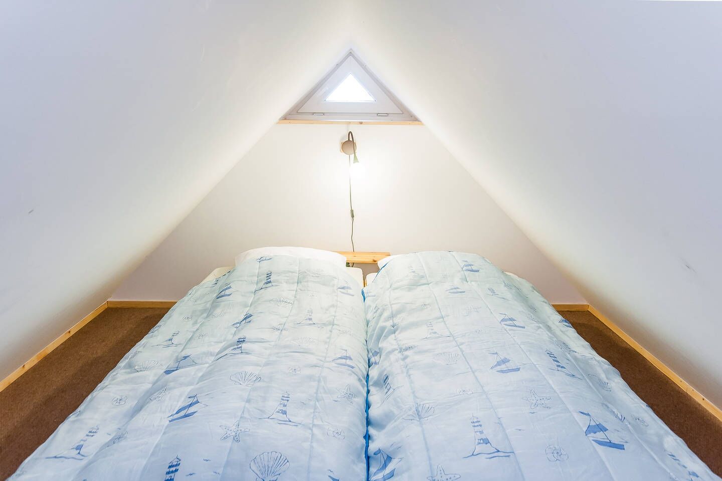 A small, triangular attic bedroom with a skylight, a bed with a nautical-themed duvet, and a wooden floor.