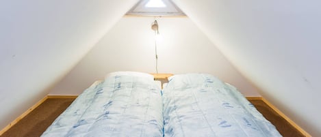 A small, triangular attic bedroom with a skylight, a bed with a nautical-themed duvet, and a wooden floor.