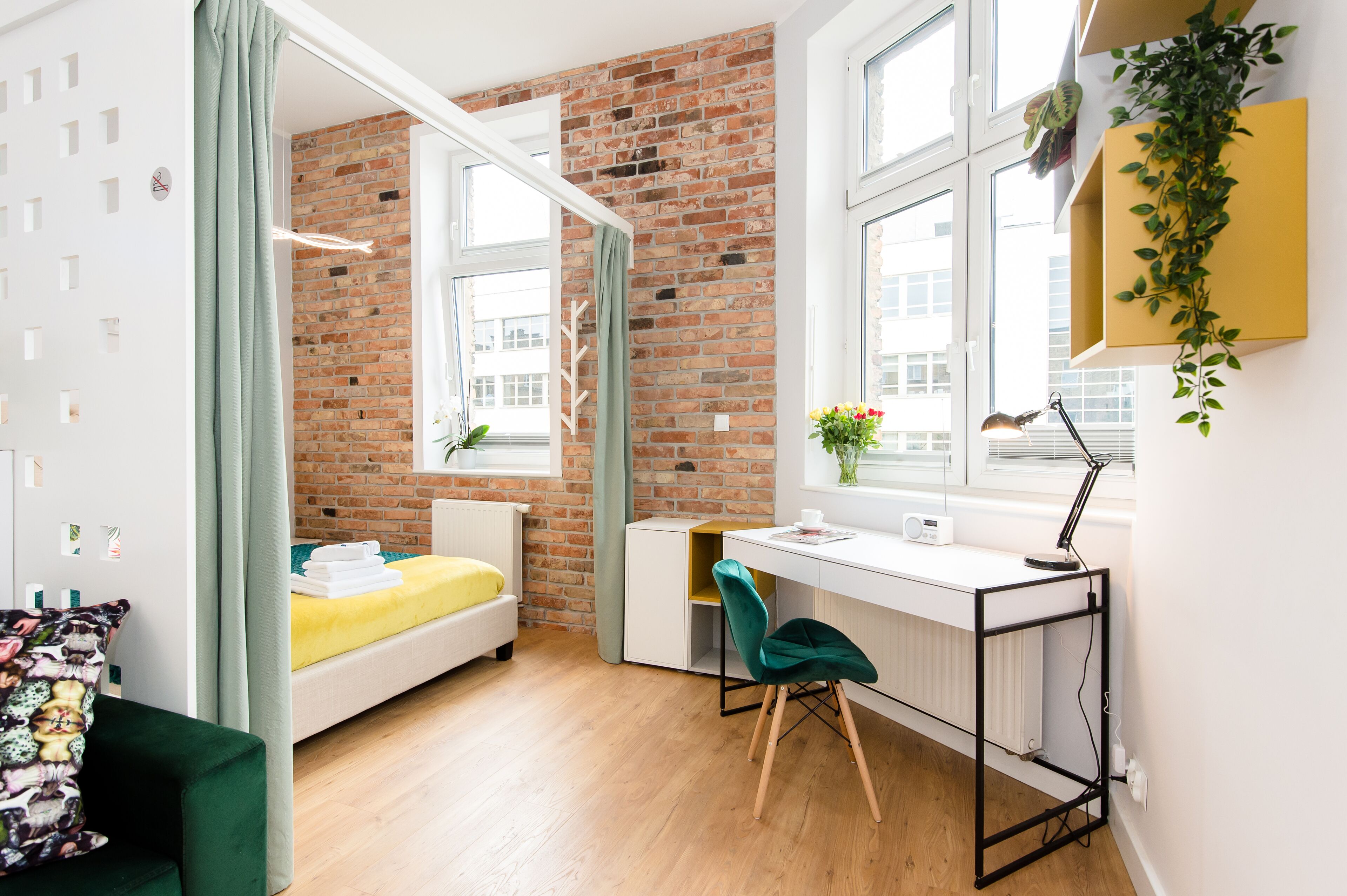 Une chambre avec un lit, un bureau, une chaise et une fenêtre donnant sur des immeubles.