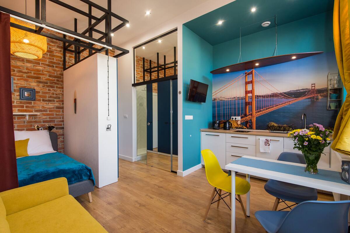 A modern room with a bed, a desk, and a chair. There is a painting of a bridge on the wall.