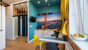 Een moderne keuken met een muurschildering van de Golden Gate Bridge, een eethoek met gele stoelen, en een raam met gordijnen.