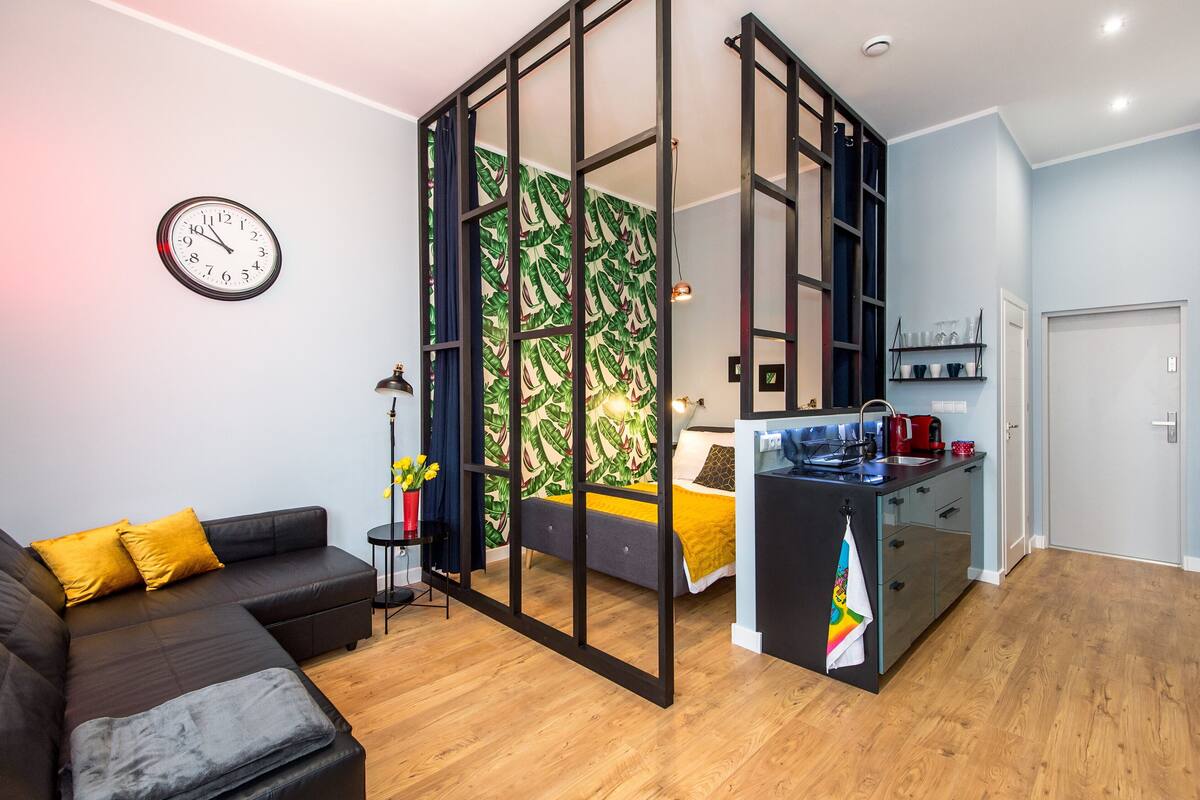 A modern living space with a sofa, a bed, a kitchen area, and a wall clock.