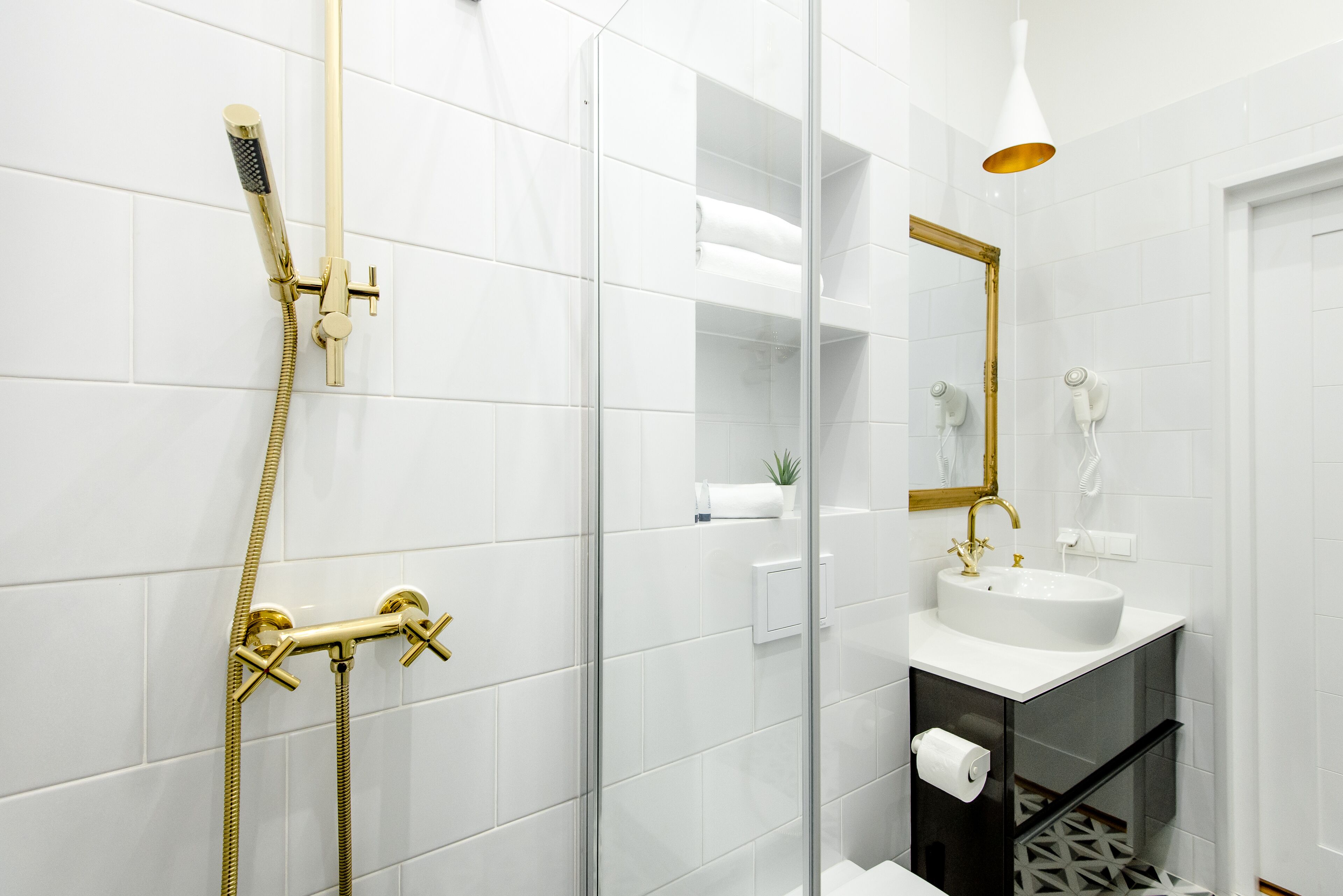 A modern bathroom with a glass shower enclosure, a gold showerhead, and a white sink with a gold faucet.