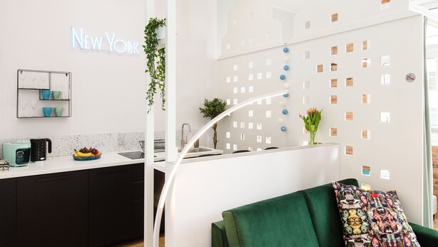 Een modern interieur met een groene bank, een keukenhoek en een muur met een 'New York'-bord.