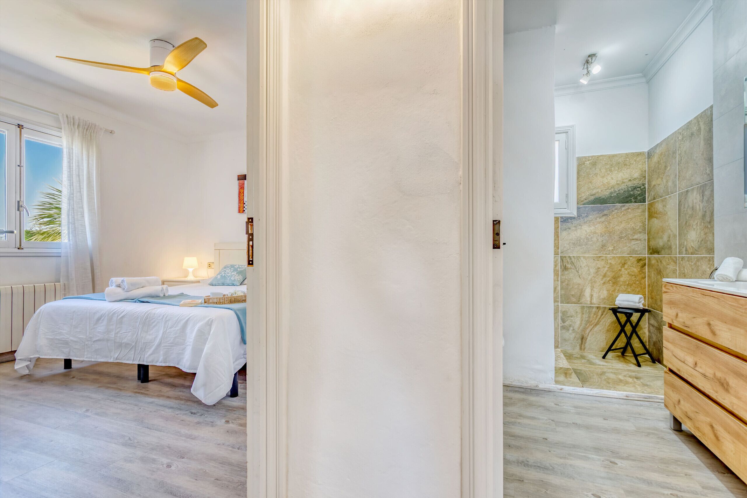 Een slaapkamer met een bed, een plafondventilator, een nachtkastje en een raam met gordijnen.