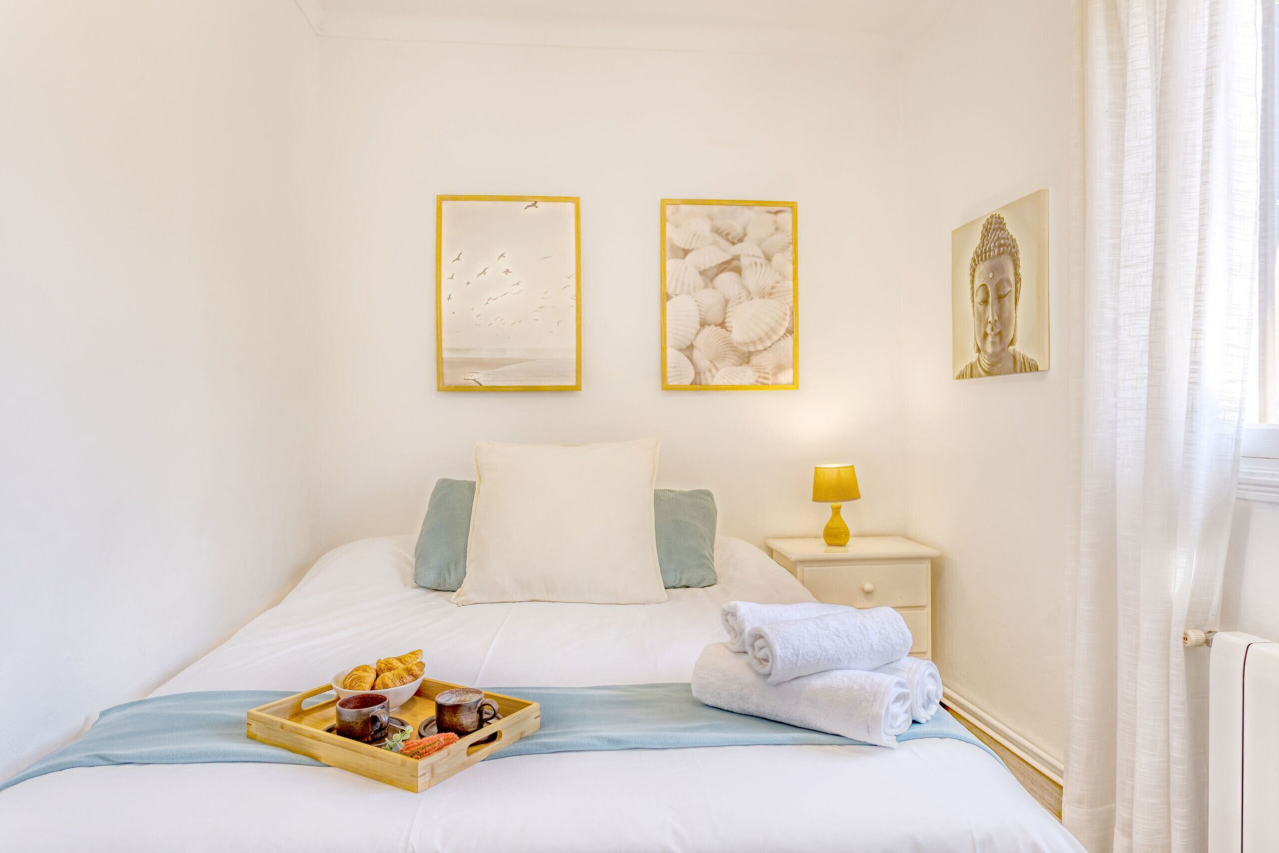 A hotel room with a bed, pillows, a bedside table with a lamp, and artwork on the walls.