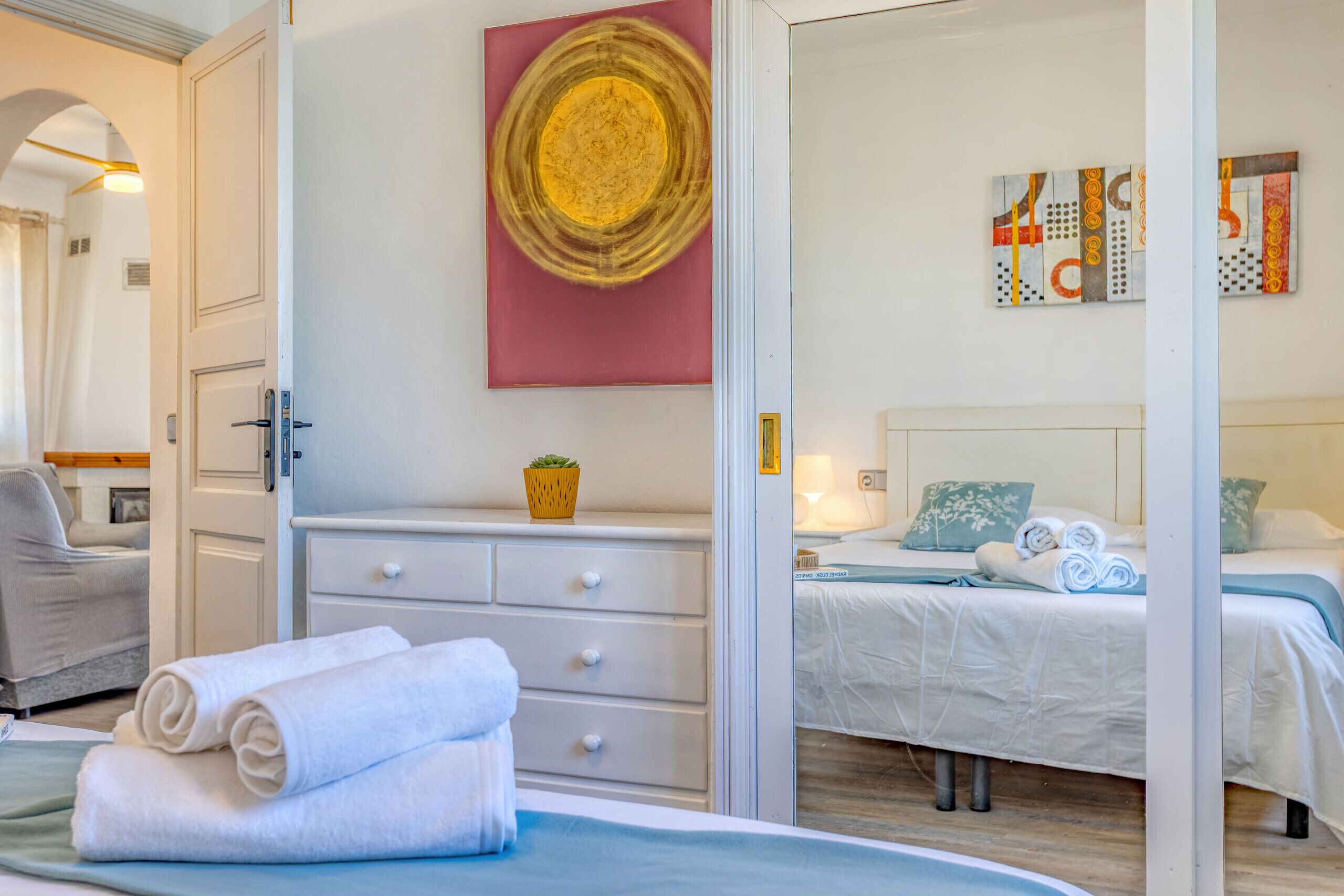 Hotelkamer met een bed, een kaptafel, een muur met kunstwerken en een zichtbare badkamer door een geopende deur.