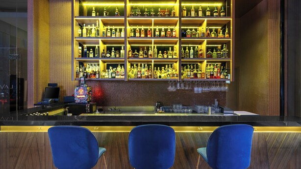 Un'area bar con scaffali pieni di bottiglie, un bancone e tre sedie blu.
