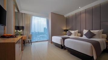 A hotel room with a desk, two beds, a TV, and a large window with curtains.