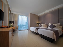 A hotel room with a desk, two beds, a TV, and a large window with curtains.