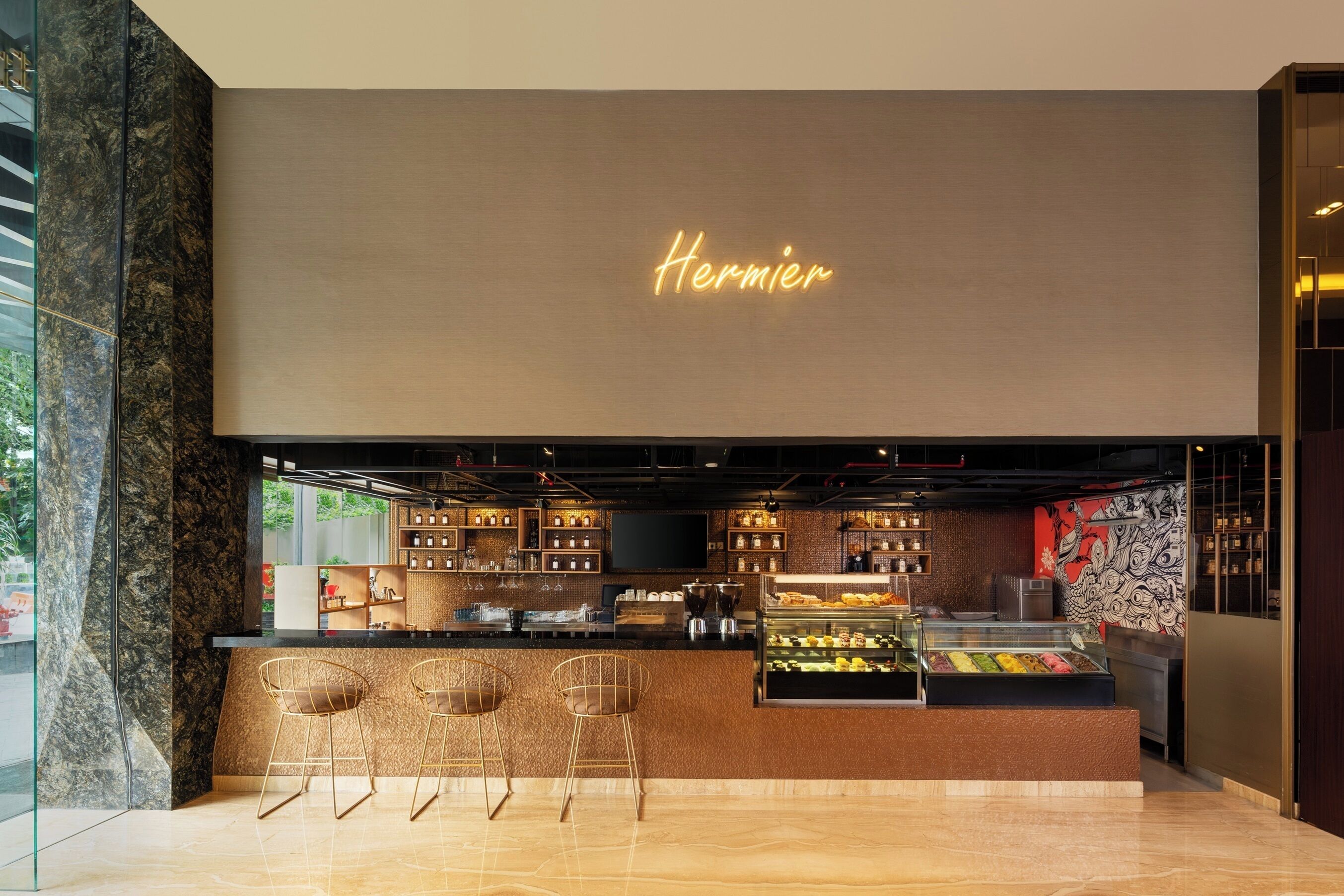Un intérieur moderne avec un panneau néon sur lequel on peut lire « Hermier », un comptoir avec une vitrine et trois tabourets de bar.