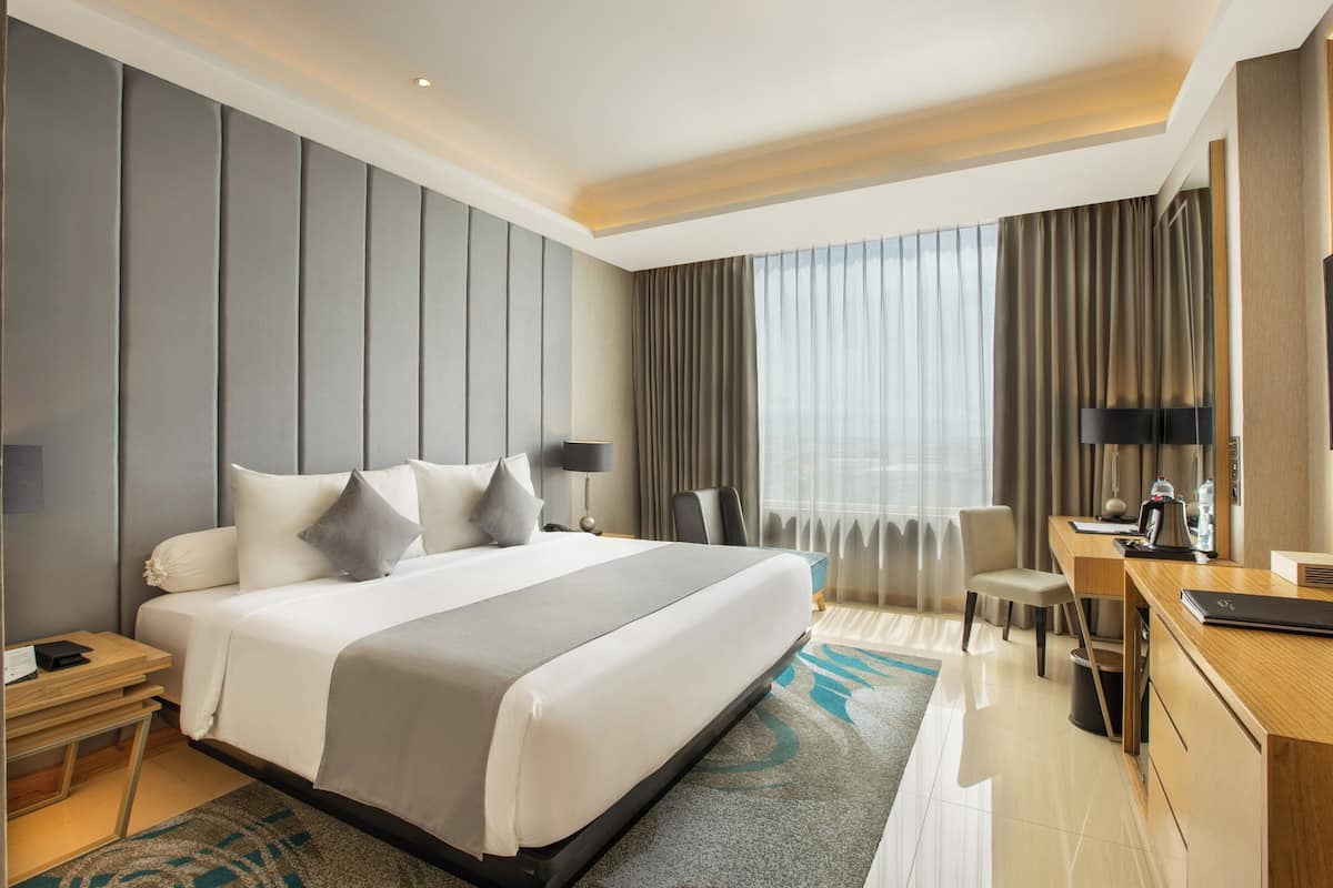 Ein modernes Hotelzimmer mit einem großen Bett, einem Schreibtisch, einem Sessel, einem Fernseher und einem Fenster mit Vorhängen.