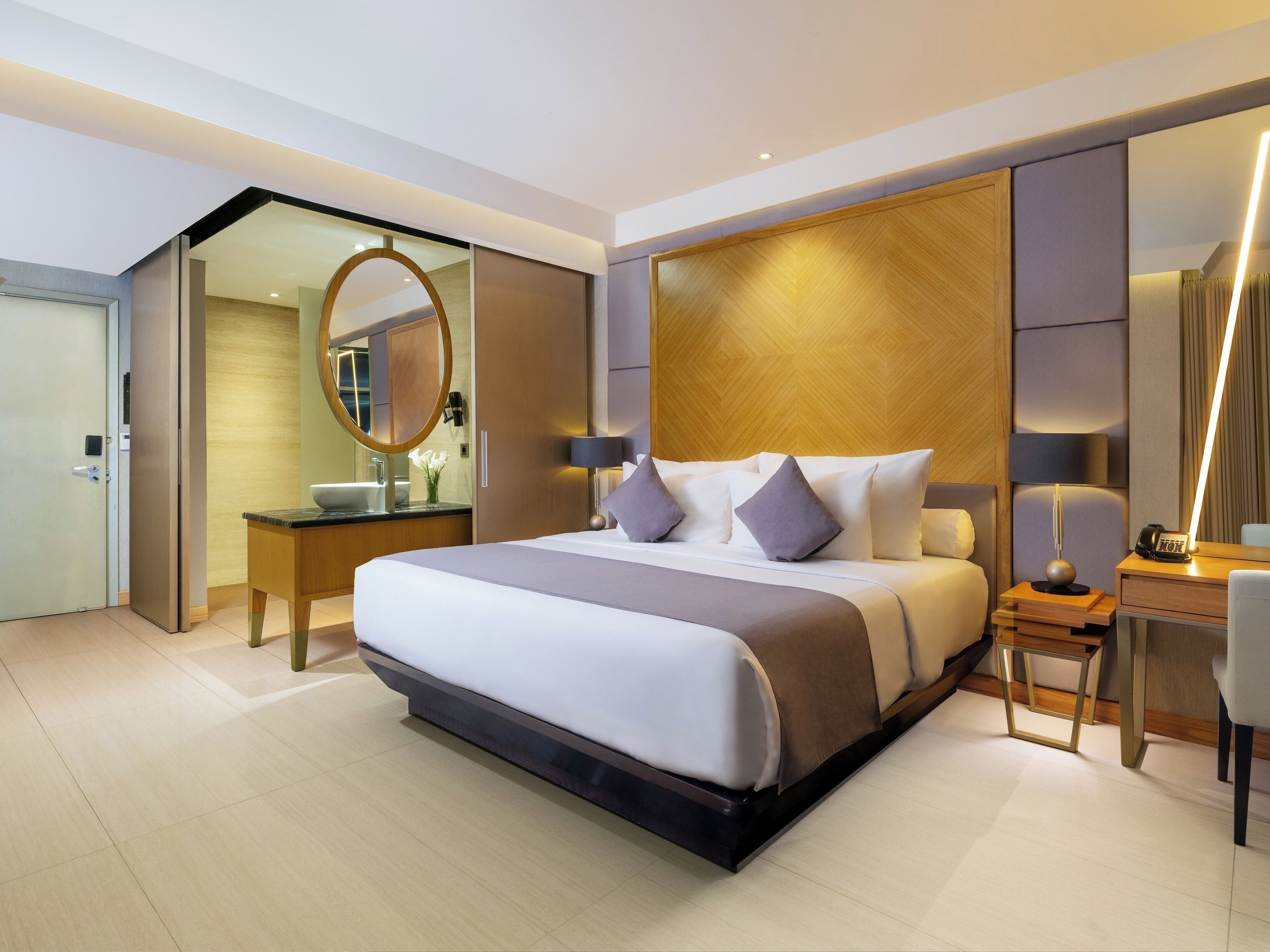 A modern hotel room with a large bed, bedside tables, a mirror, and a desk with a lamp.