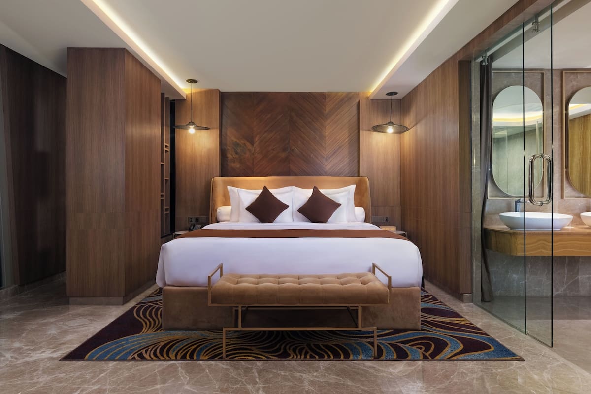 Ein modernes Hotelzimmer mit einem großen Bett, einer Bank, einer Duschkabine aus Glas und einem Marmorboden.
