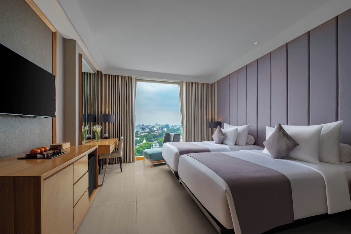 Ein Hotelzimmer mit einem großen Bett, einem Schreibtisch, einem Fernseher und Blick auf die Stadt.