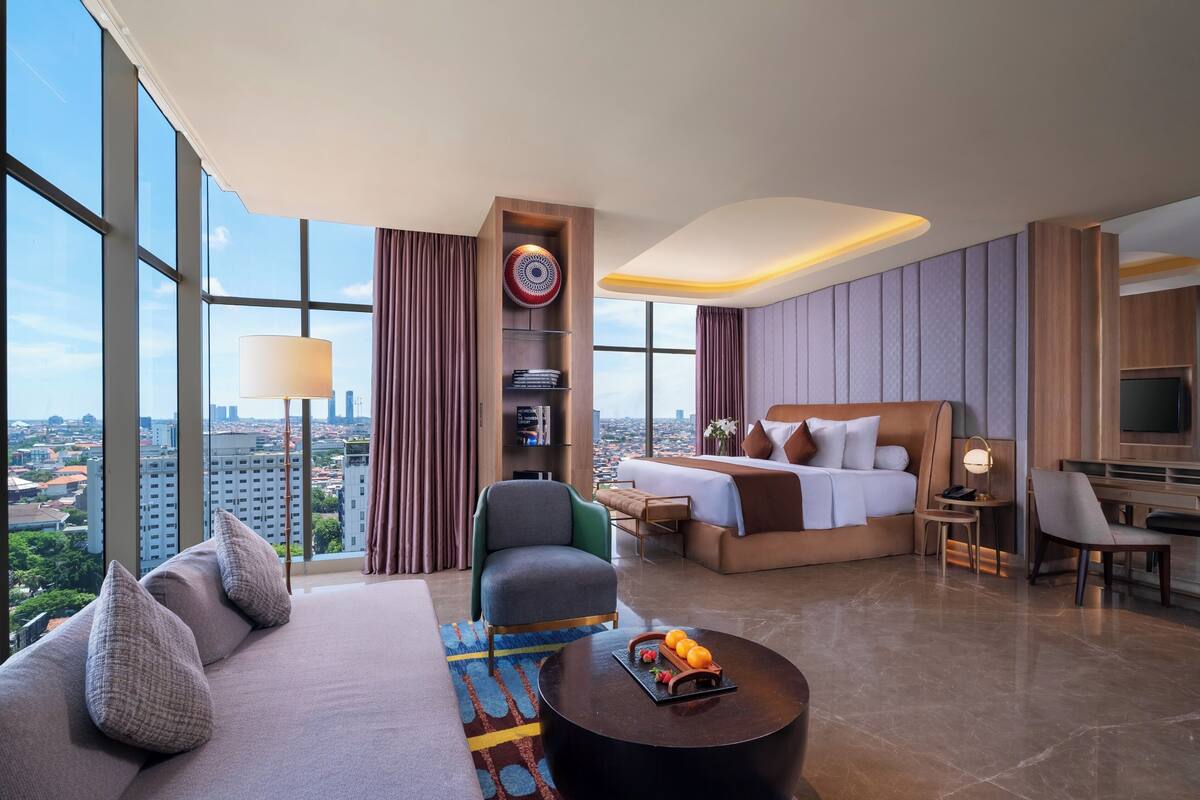 Ein Hotelzimmer mit großem Fenster, einer Couch, einem Bett, einem Schreibtisch und einem Fernseher.