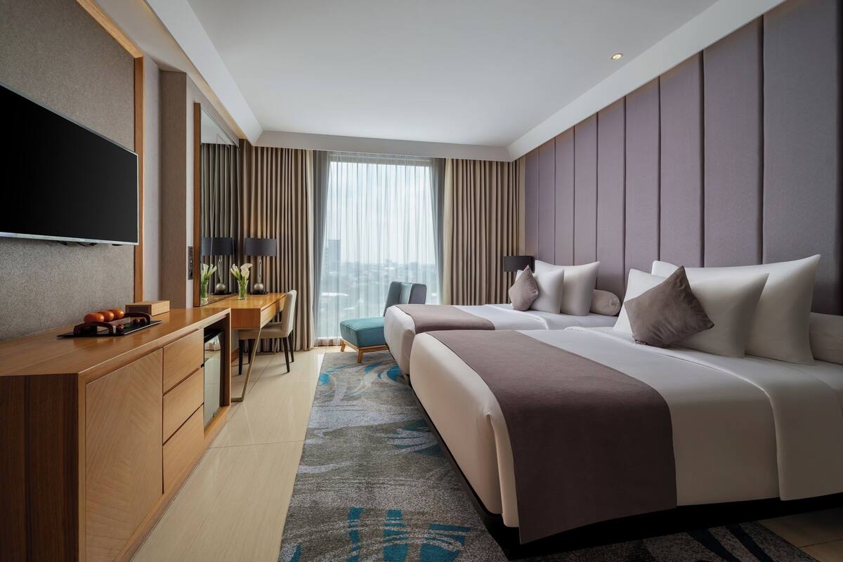 Ein modernes Hotelzimmer mit einem großen Bett, einem Schreibtisch, einem Fernseher und Blick auf die Stadt.