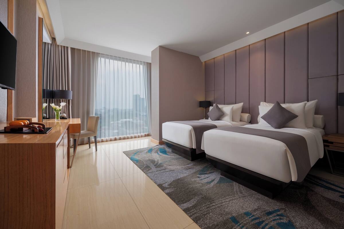 Ein Hotelzimmer mit einem Bett, einem Schreibtisch, einem Stuhl, einem Fernseher und einem großen Fenster mit Vorhängen.