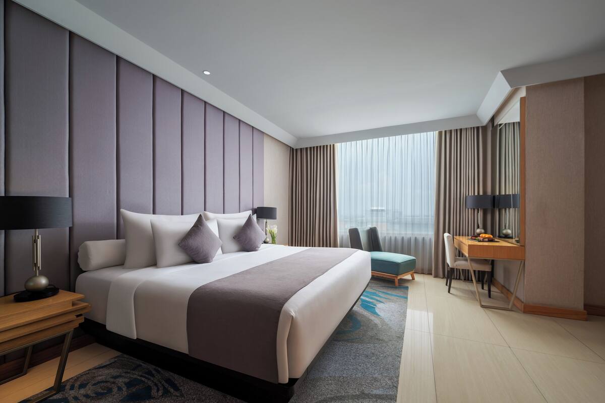 Ein modernes Hotelzimmer mit einem großen Bett, einem Schreibtisch und Blick auf die Stadt.