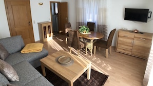 A living room with a sofa, a coffee table, a dining table with chairs, a TV, and a cabinet. - Apartment Almrausch 75sqm, balcony, kitchen, 1 bedroom, 1 living room, WLAN (Ruhpolding)