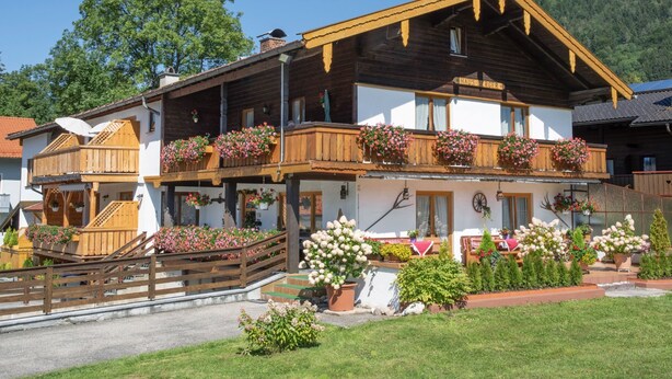 A traditional wooden chalet with balconies adorned with flowers, a wooden deck, and a well-maintained garden. - Apartment Almrausch 75sqm, balcony, kitchen, 1 bedroom, 1 living room, WLAN (Ruhpolding)