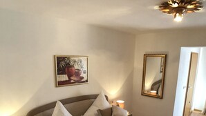 A spacious bedroom with a large bed, bedside lamps, a wall-mounted mirror, and a painting. - Apartment Almrausch 75sqm, balcony, kitchen, 1 bedroom, 1 living room, WLAN (Ruhpolding)