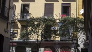 Un edificio de varios pisos con balcones, locales comerciales y peatones.