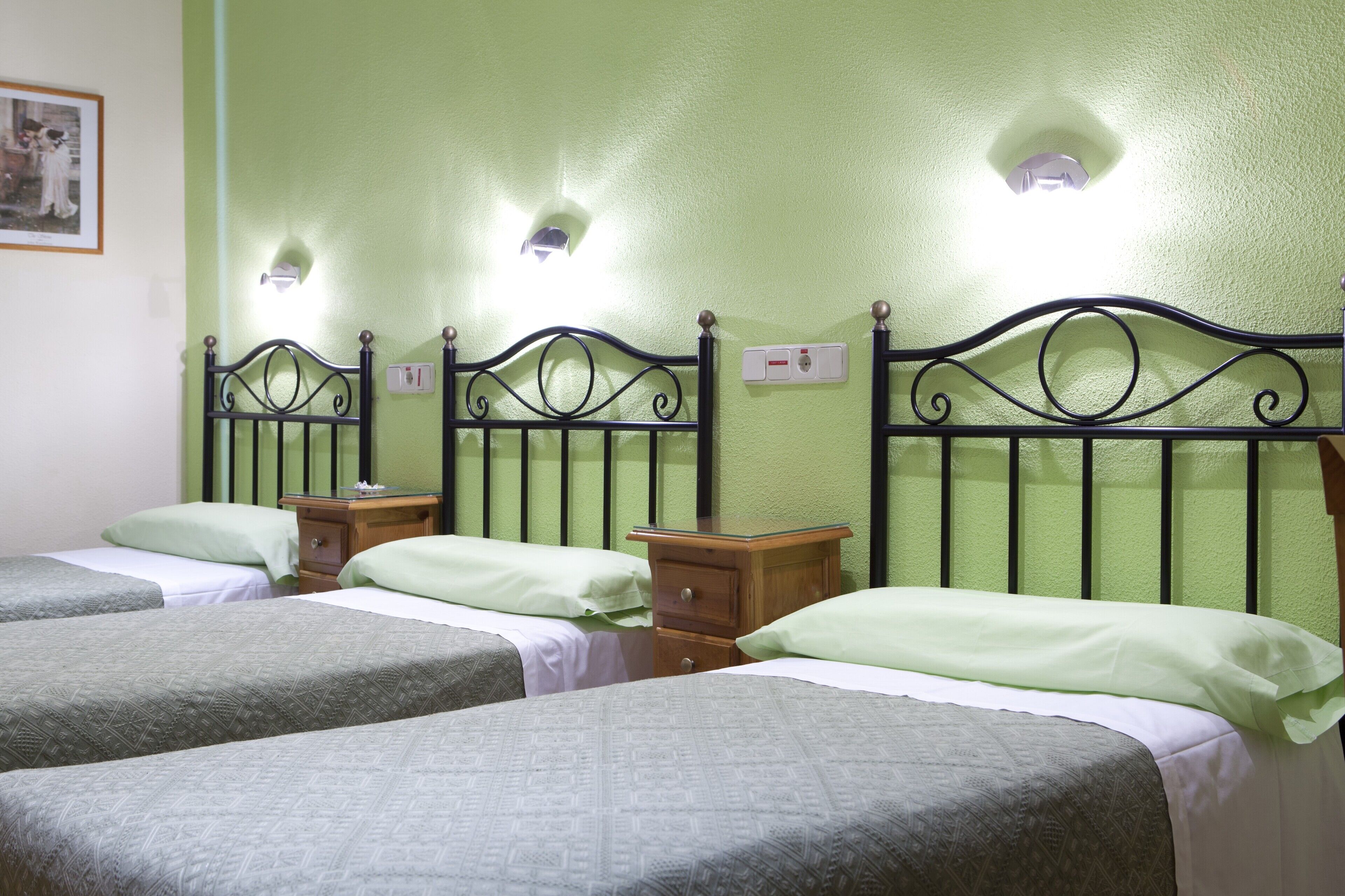Una habitación con tres camas, cada una con una mesita de noche de madera y un interruptor de luz en la pared.