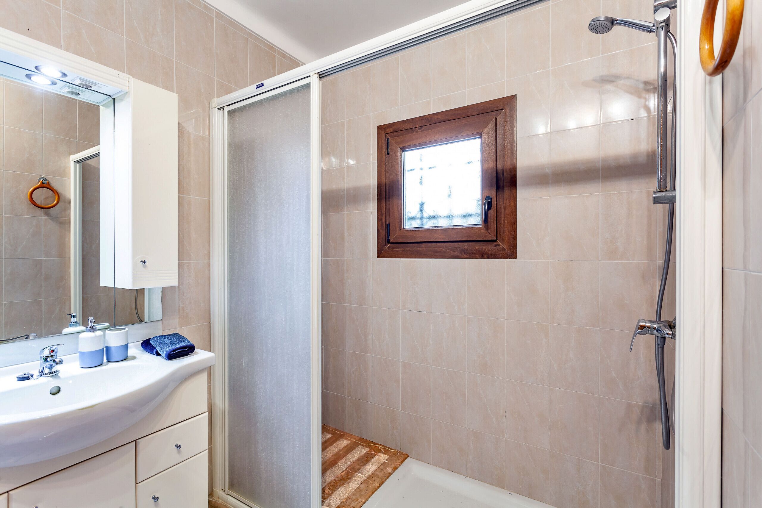 A bathroom with a sink, mirror, shower, and a small window.