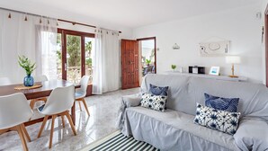 Una sala de estar moderna con un sofá gris, sillas blancas, una mesa de comedor de madera y un amplio ventanal con cortinas.