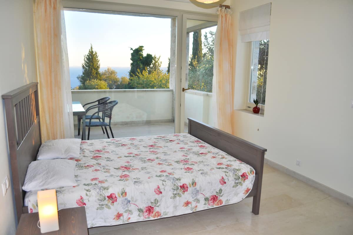 Un dormitorio con cama, una silla, una mesa y vistas a árboles y al cielo.