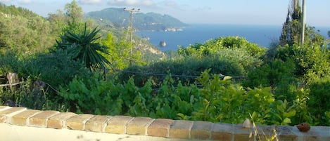 A terrace with a view of the sea and hills, a tiled floor, and a railing.