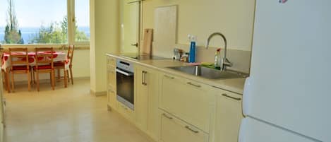 Una cocina con una mesa de comedor, sillas, refrigerador, lavabo y ventana con vistas.