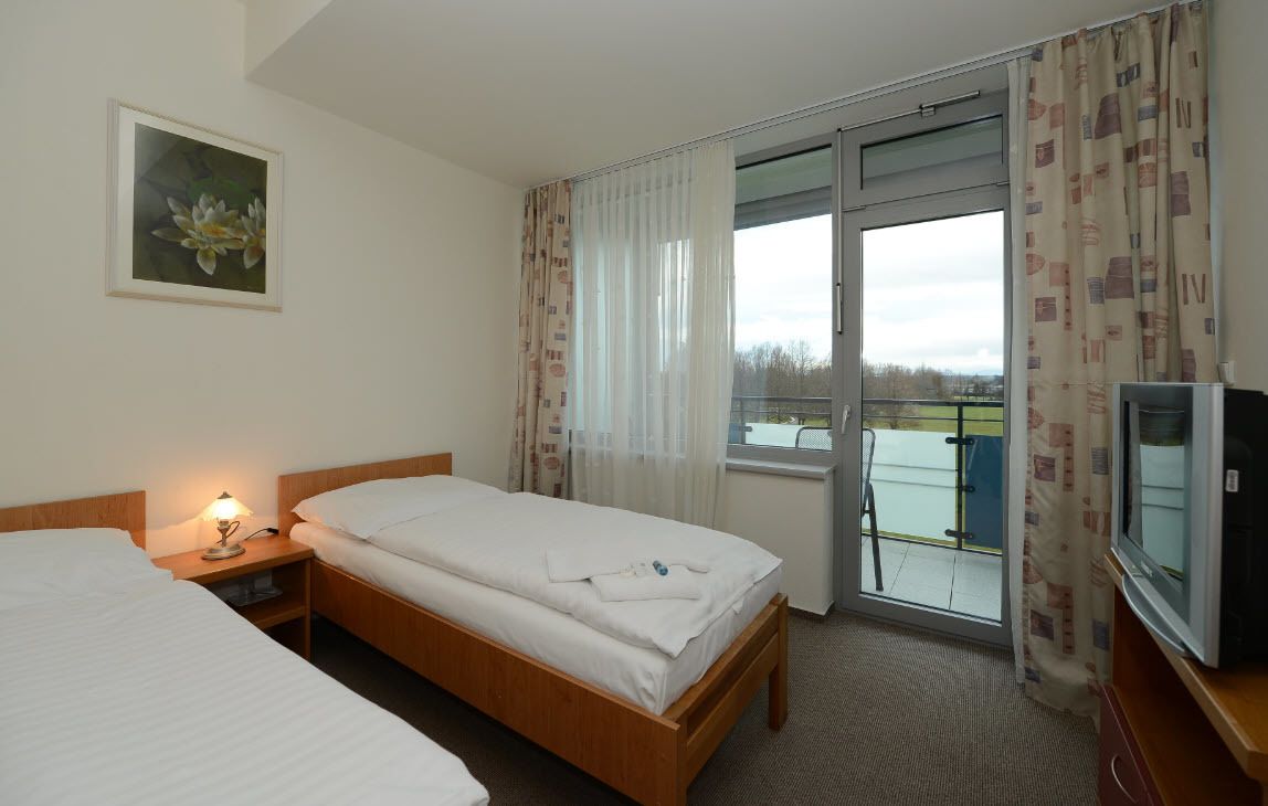 A hotel room with two beds, a TV, a painting, and a balcony with curtains.