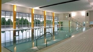 En moderne indendørs swimmingpool med glasvægge, flisegulv og en trappe, der fører til et plan over.