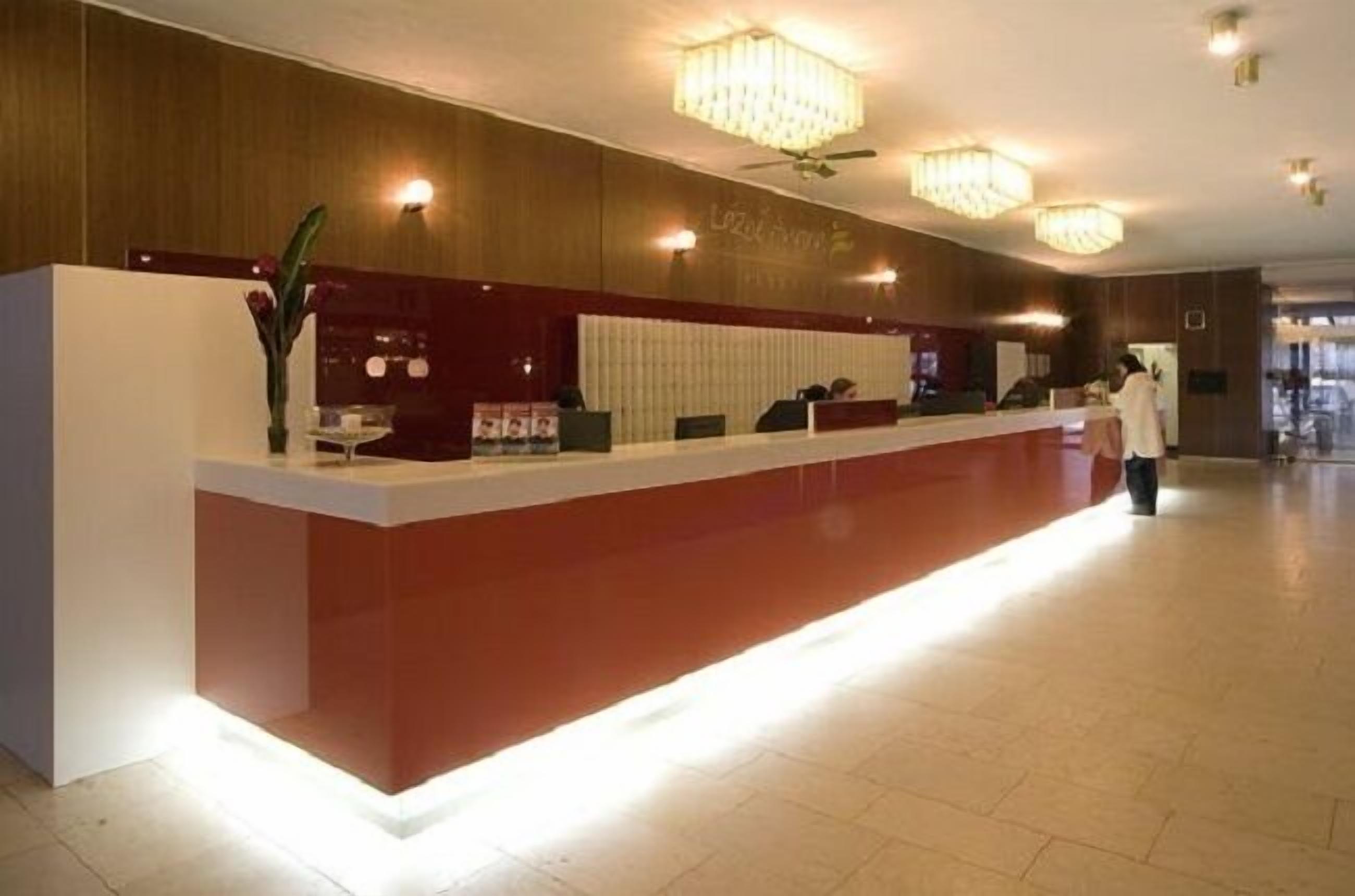 A hotel reception area with a modern design, featuring a reception desk, a chandelier, and a large window.