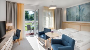 Et hotelværelse med en seng, to blå lænestole, et lille bord med en vase, et fjernsyn og et billede på væggen.