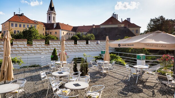 En terrasse med udendørs siddepladser, et tårn med et ur og en bygning med facade af fliser.