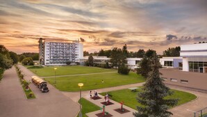 Et hotel med en stor parkeringsplads, et græsområde med træningsudstyr og en bygning med flere etager og altaner.