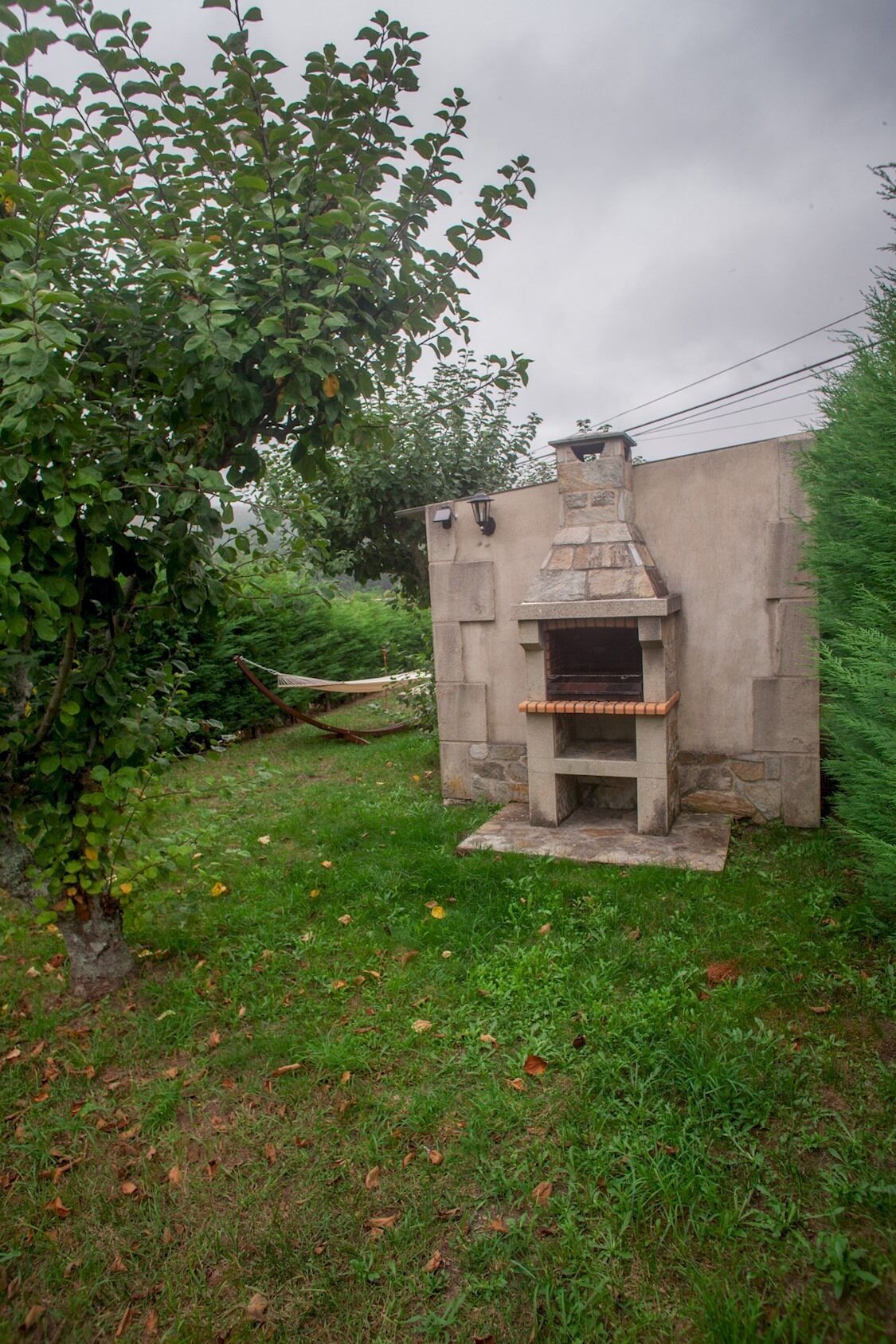 Un horno de piedra al aire libre con chimenea, rodeado de césped y árboles.