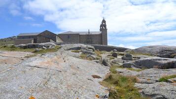 Un edificio de piedra con un campanario, rodeado de rocas grandes y vegetación escasa.
