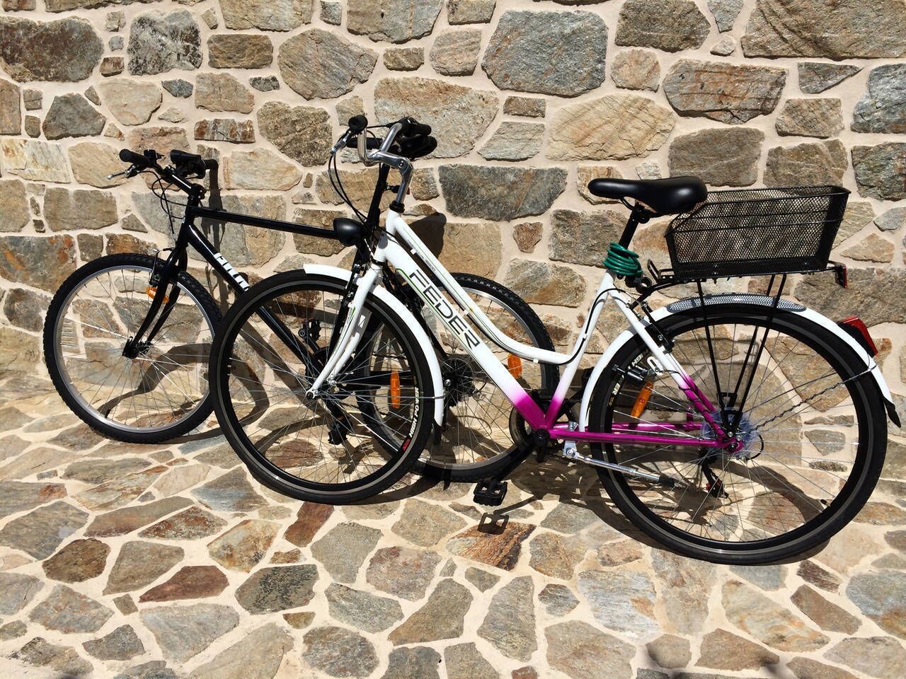 Dues bicicletes aparcades davant d'una paret de pedra.