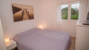 A bedroom with a bed, bedside lamps, a desk with a computer, a window with a view of greenery, and a painting on the wall. - Casa de Piedra Playa de Estorde con vistas al mar (Cee)